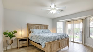 Une chambre à coucher avec un lit en bois, une table de chevet, une plante en pot et un ventilateur de plafond.