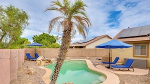 Un jardin avec une piscine, un palmier, des chaises longues et des panneaux solaires.