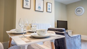 Een eethoek met een tafel gedekt voor twee personen, een klok aan de muur en kunstwerken in lijsten erboven.