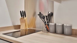 A kitchen counter with a built-in induction cooktop, a wooden knife block, a utensil holder, and three grey containers labeled "SUGAR," "TEA," and "COFFEE." - WhiskAwayHomes Jenkins House Apartment 2 (Worcestershire)