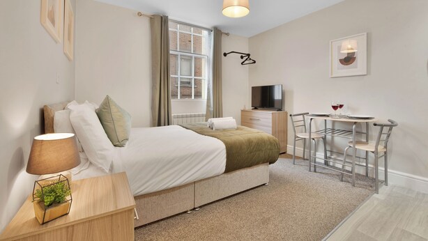 A bedroom with a bed, bedside table, lamp, TV, desk, chairs, and a window. - WhiskAwayHomes Jenkins House Apartment 2 (Worcestershire)