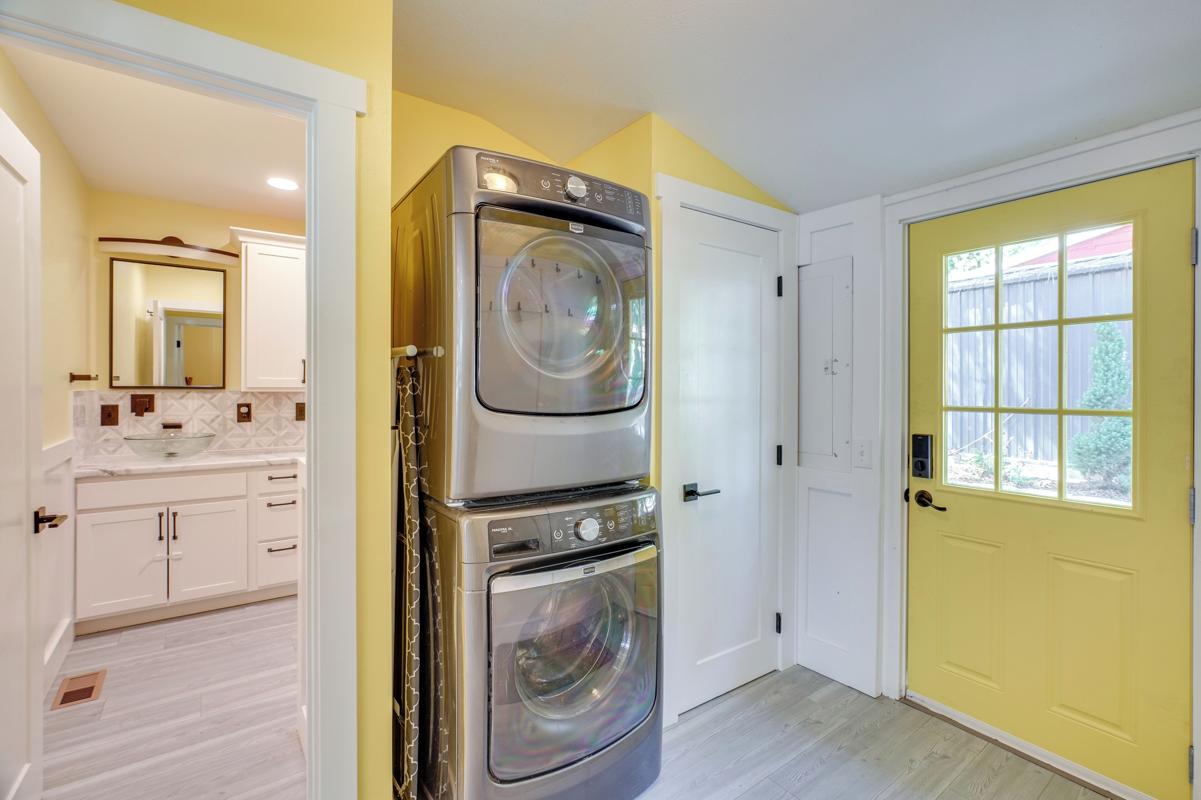 A laundry room with a stacked washer and dryer, a white door, and a yellow wall.