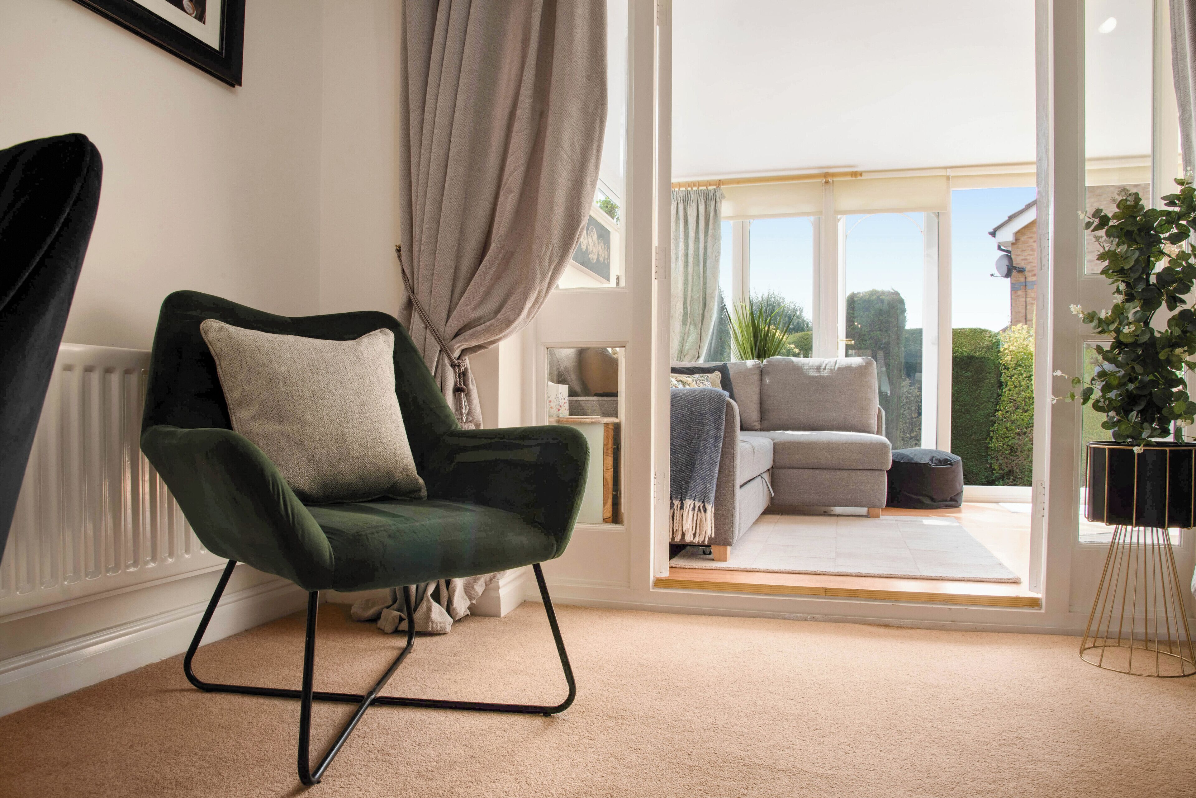 A cozy living room with a green armchair, a grey sofa, and a large window offering a view of the outdoors.