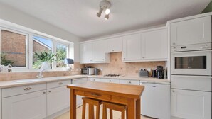 A modern kitchen with white cabinets, a wooden bar stool, a built-in oven, and a window with a view of greenery.