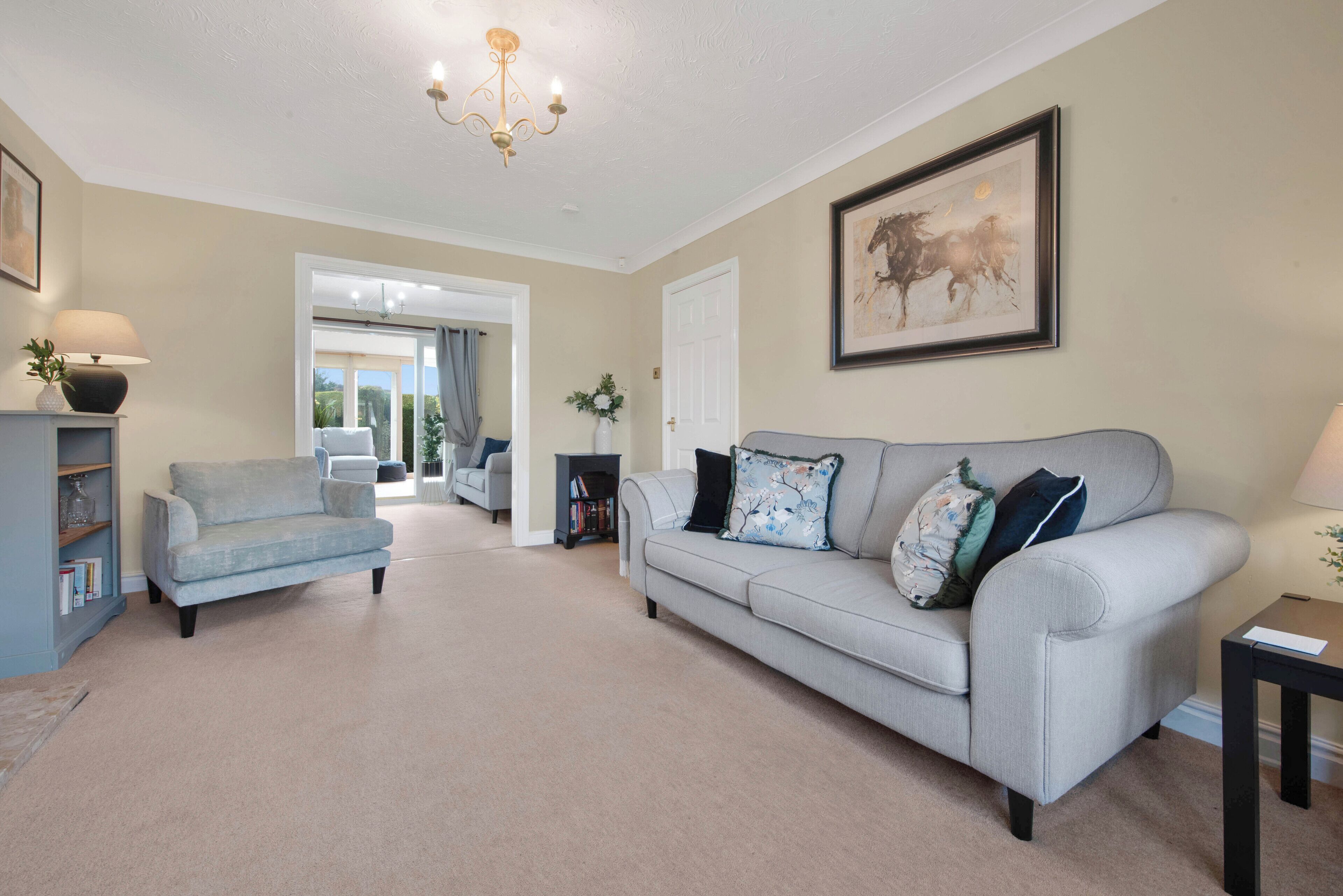 A living room with a grey sofa, a blue armchair, a chandelier, and a framed artwork on the wall.
