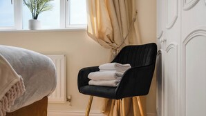A room with a bed, a black chair with gold legs, a radiator, a window with a plant, and a curtain.