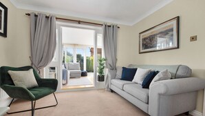 A living room with a green armchair, a grey sofa, and a large window with curtains.
