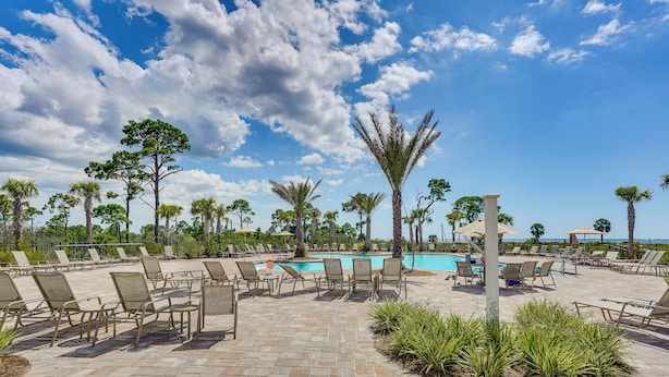 Un espace aménagé au bord de la piscine, avec des chaises longues, une piscine et des palmiers.
