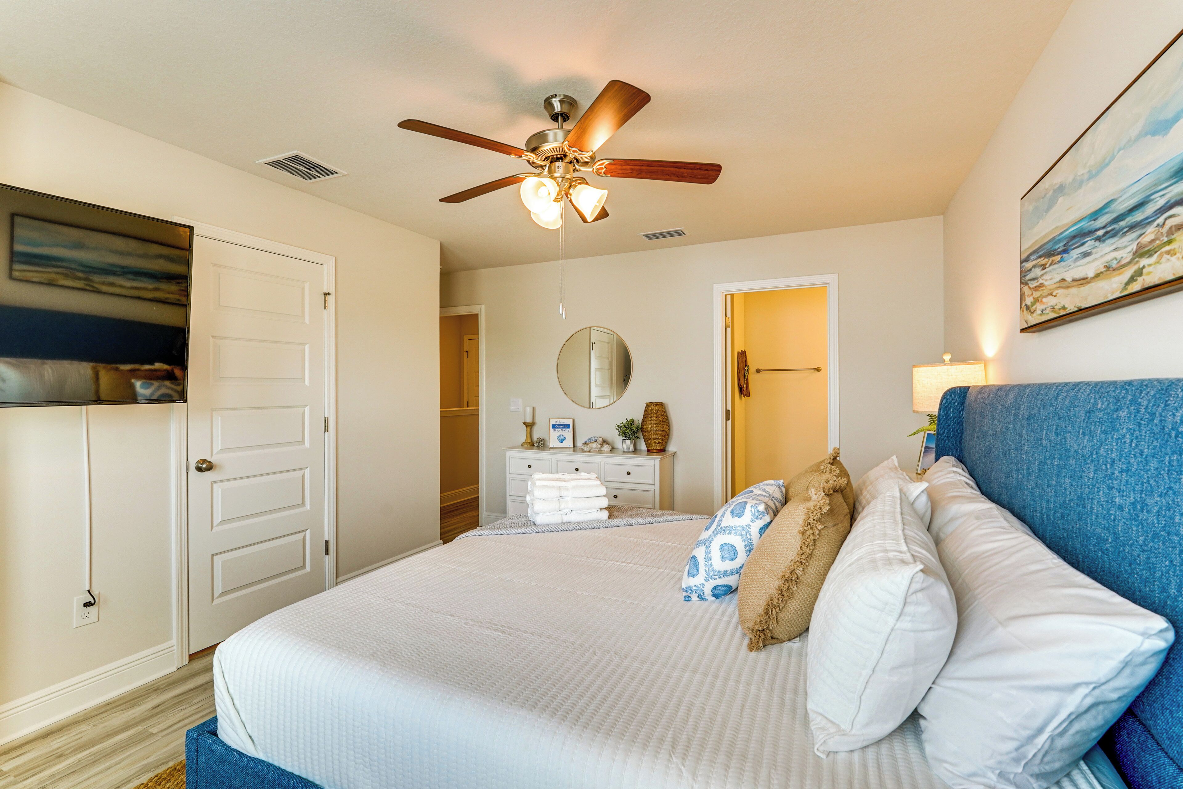 A bedroom with a bed, a ceiling fan, a dresser, a mirror, and a painting on the wall.