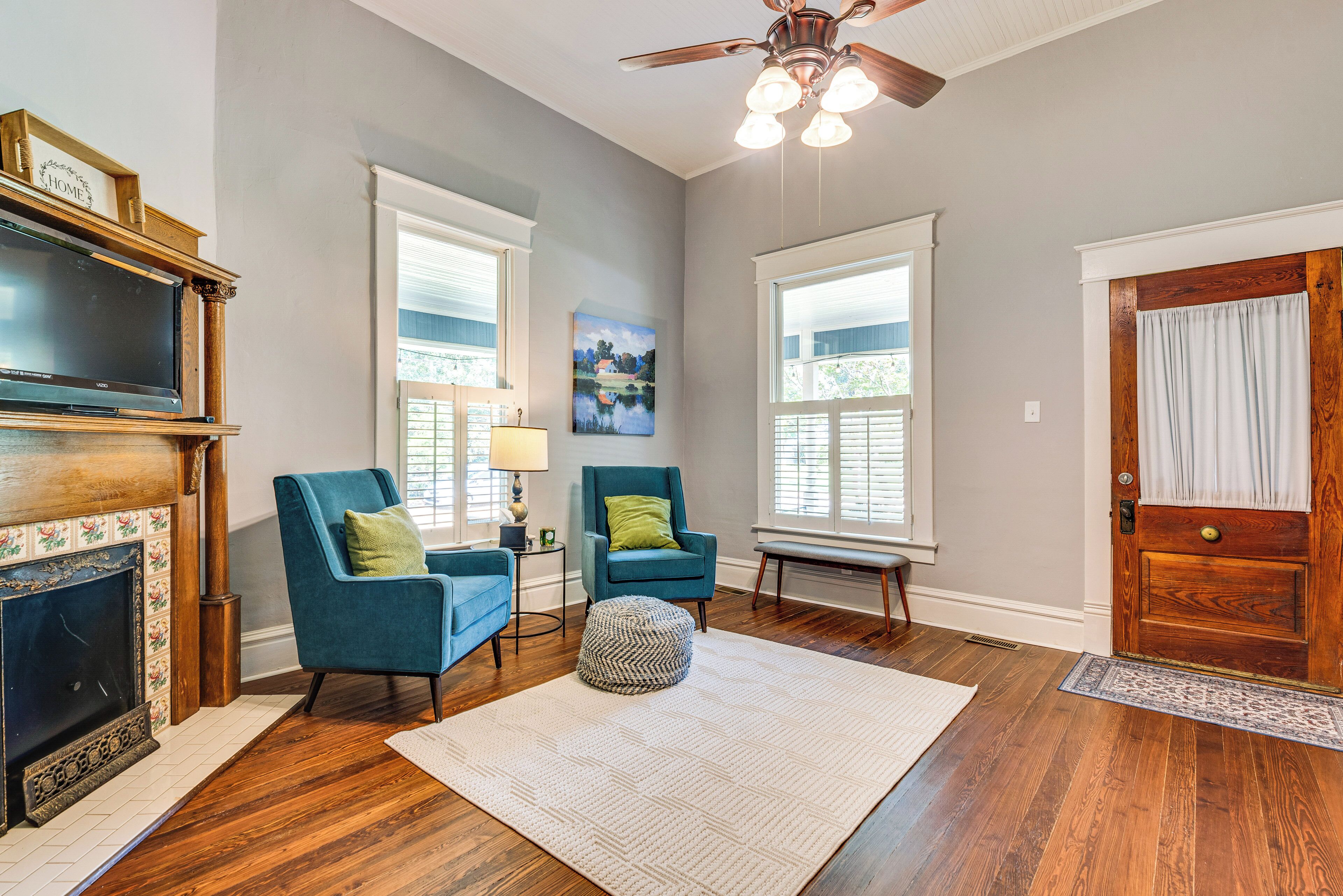 A living room with a fireplace, two blue armchairs, a rug, and a ceiling fan.