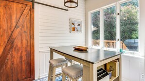 A kitchen with a wooden table, two barstools, a hanging light fixture, and a window with a view of trees. - Walk to Mcdonough Square: Historic Home w/ Yard! (McDonough)