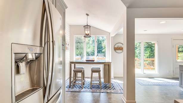 A modern kitchen with a stainless steel refrigerator, a built-in water dispenser, and a dining area with a wooden table and two stools. - Walk to Mcdonough Square: Historic Home w/ Yard! (McDonough)