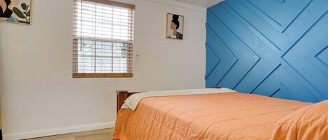 A bedroom with a bed, a window, and a blue accent wall.