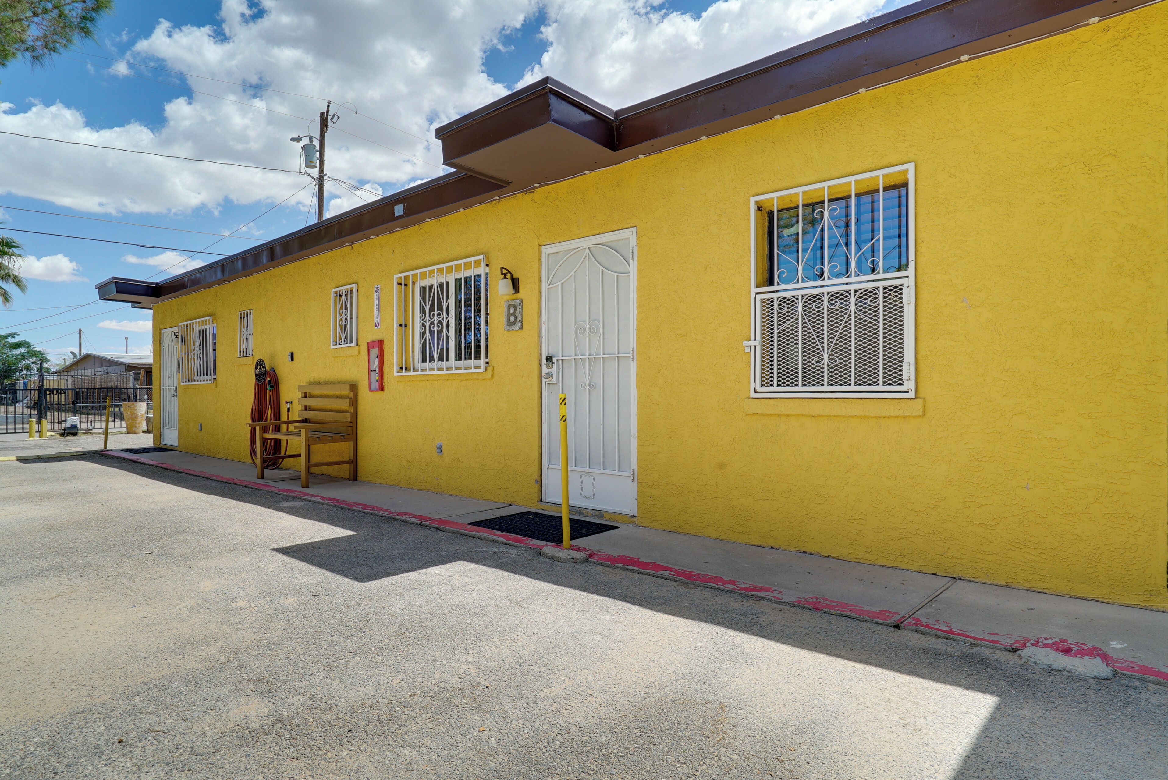 A yellow building with a red door, a bench outside, and a clear sky.
