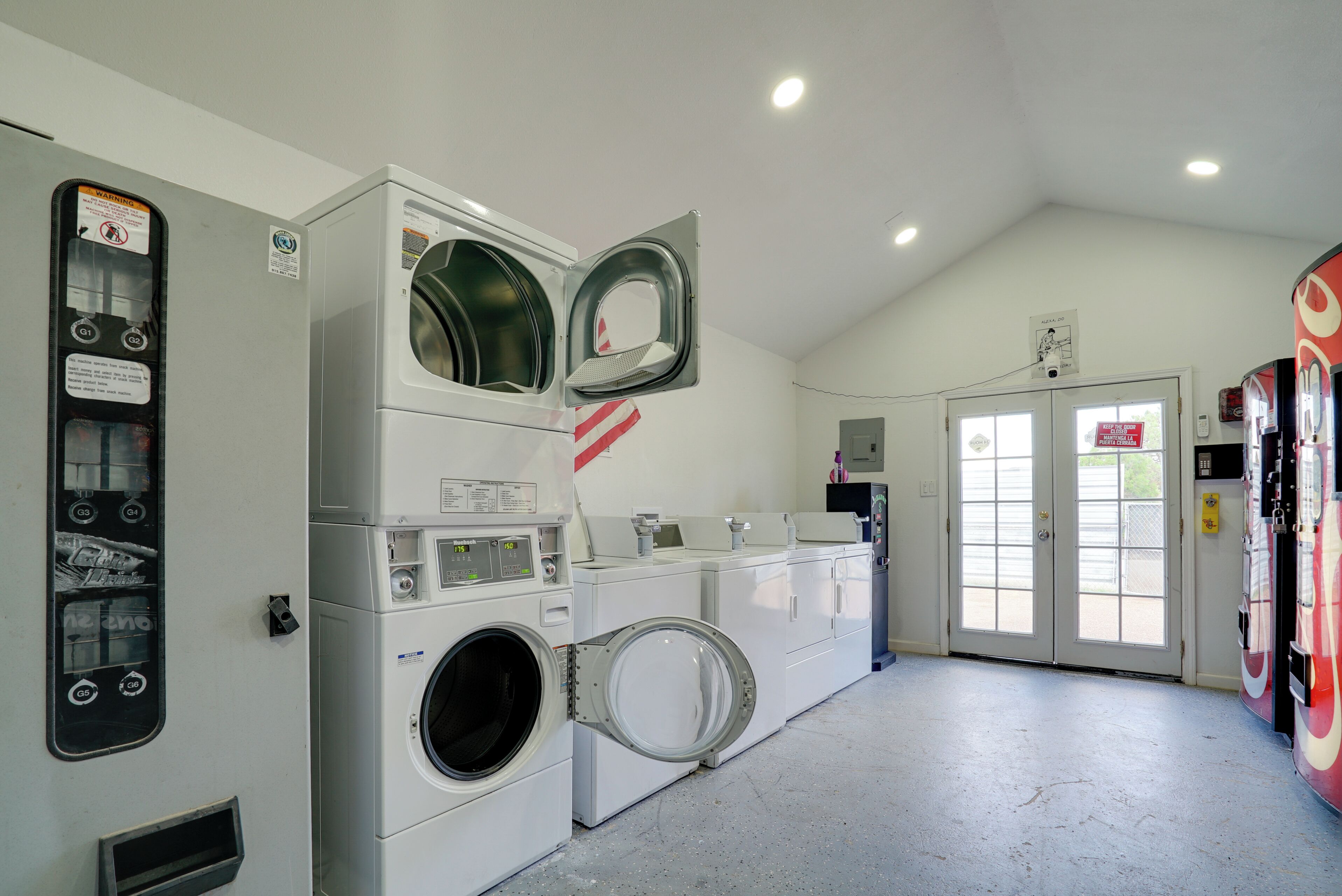 Une laverie équipée de plusieurs machines à laver et de plusieurs sèche-linge, d’un panneau de commande et d’une porte sur laquelle est apposée une pancarte.