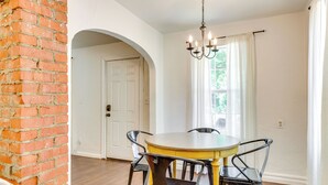 A dining area with a round table and four chairs, a chandelier, and a window with curtains.