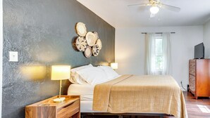 A bedroom with a bed, bedside tables, a ceiling fan, a wall-mounted decorative piece, a dresser, and a window with curtains.