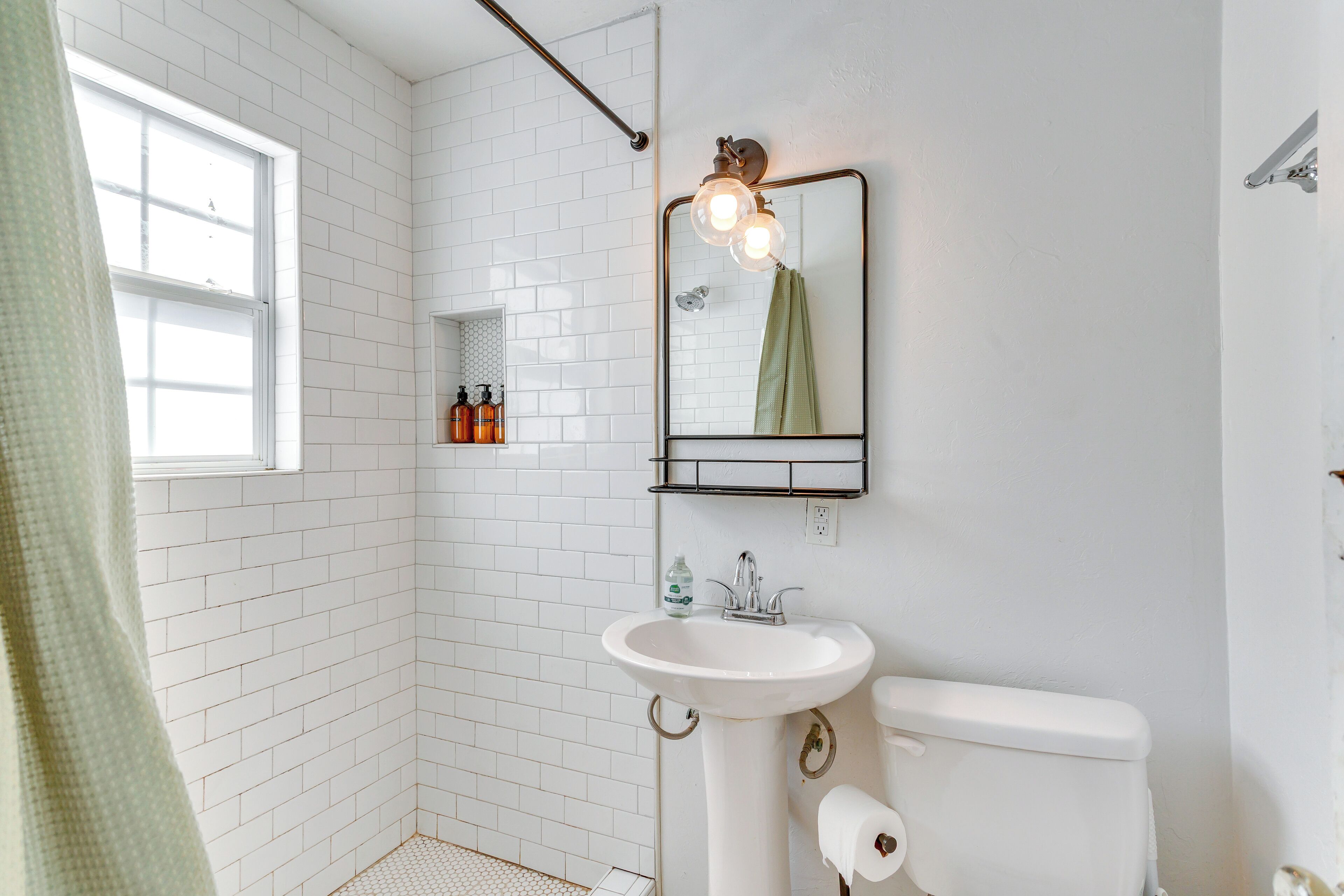 Een badkamer met witte metrotegels, een witte wastafel, een toilet, een spiegel met verlichting en een raam.