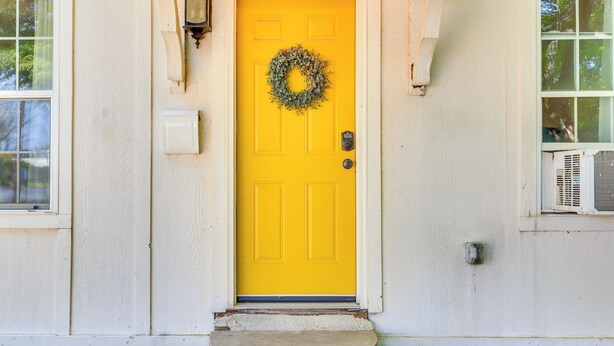 A yellow door with a wreath, a light fixture, and a small step leading up to the entrance.
