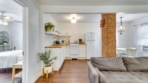 A modern kitchen with white cabinets, a brick column, and a dining area with a table and chairs. - Heart of OKC Plaza District: Duplex Near Shops! (Oklahoma City)