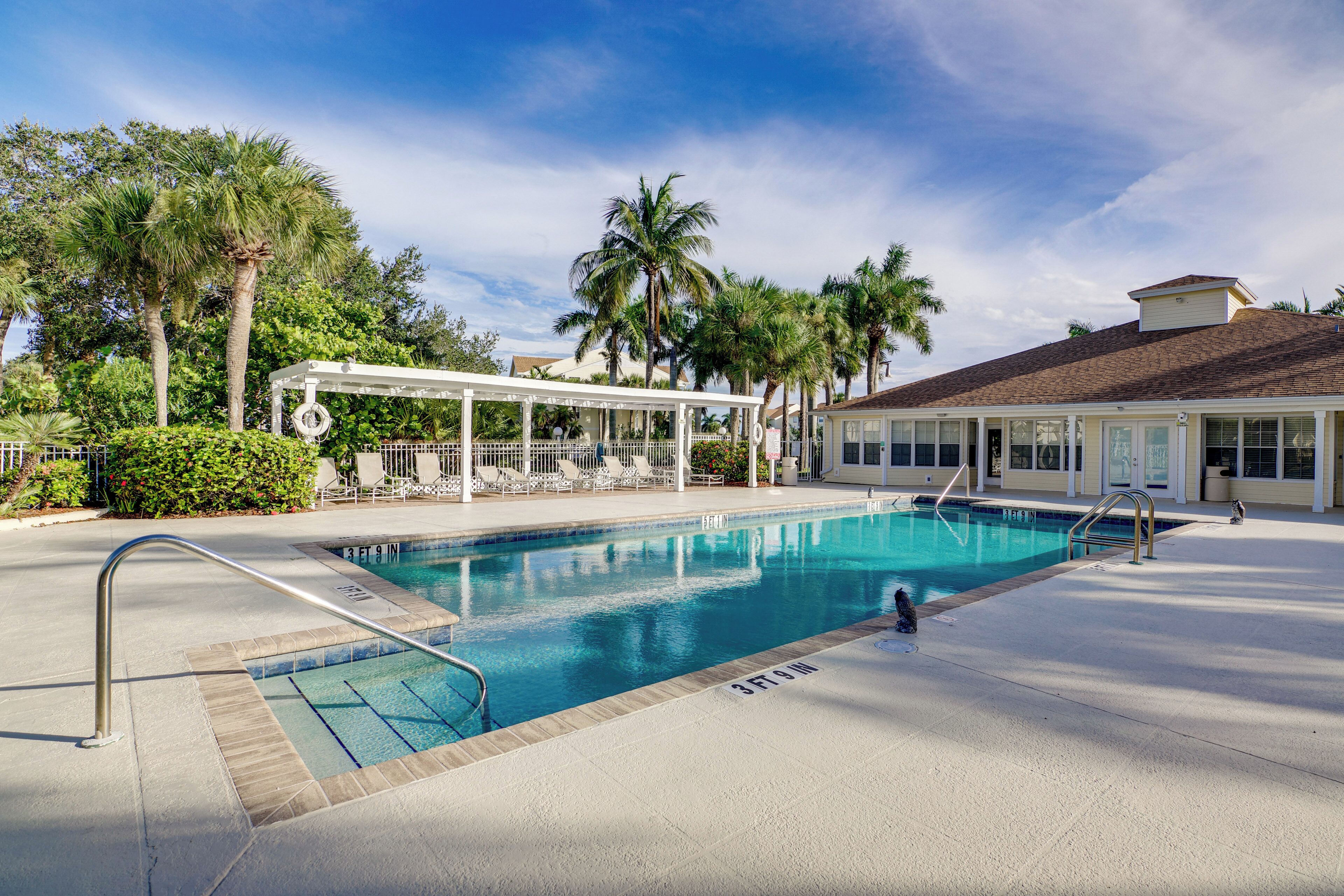 A swimming pool with a sun deck, palm trees, and a covered seating area.