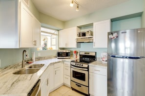 A modern kitchen with white cabinets, stainless steel appliances, a sink, and a window with blinds. - Walk to Beach: 1st-floor Unit w/ Pool in Melbourne (Indialantic)