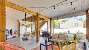 Une terrasse extérieure couverte avec des poutres en bois, une table agrémentée d’une plante en pot, des chaises orange et un canapé.