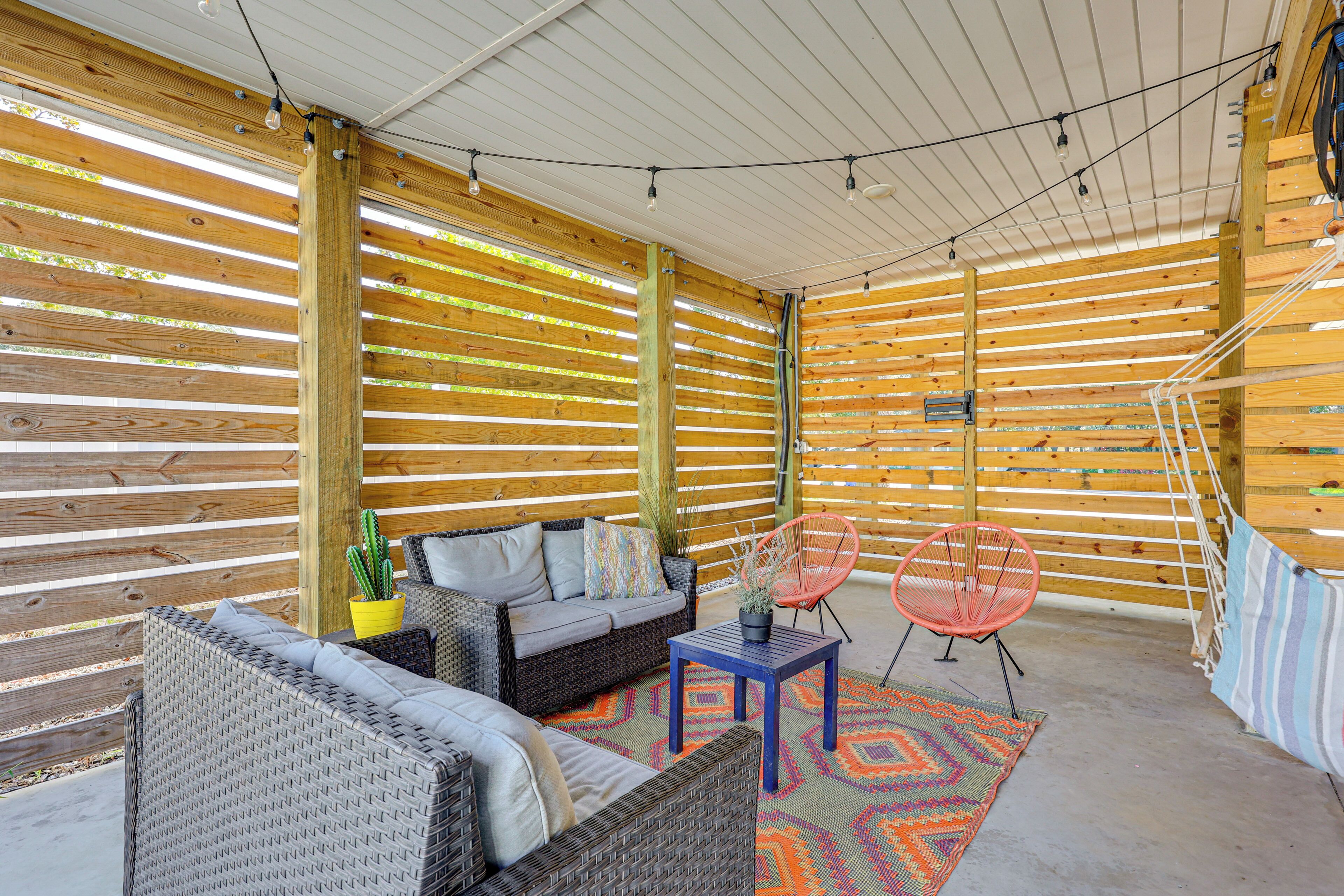 An outdoor patio area with wicker furniture, a colorful rug, and a wooden slatted ceiling.