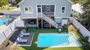 Une maison à deux étages avec une piscine dans le jardin, une terrasse en bois et un patio clos.