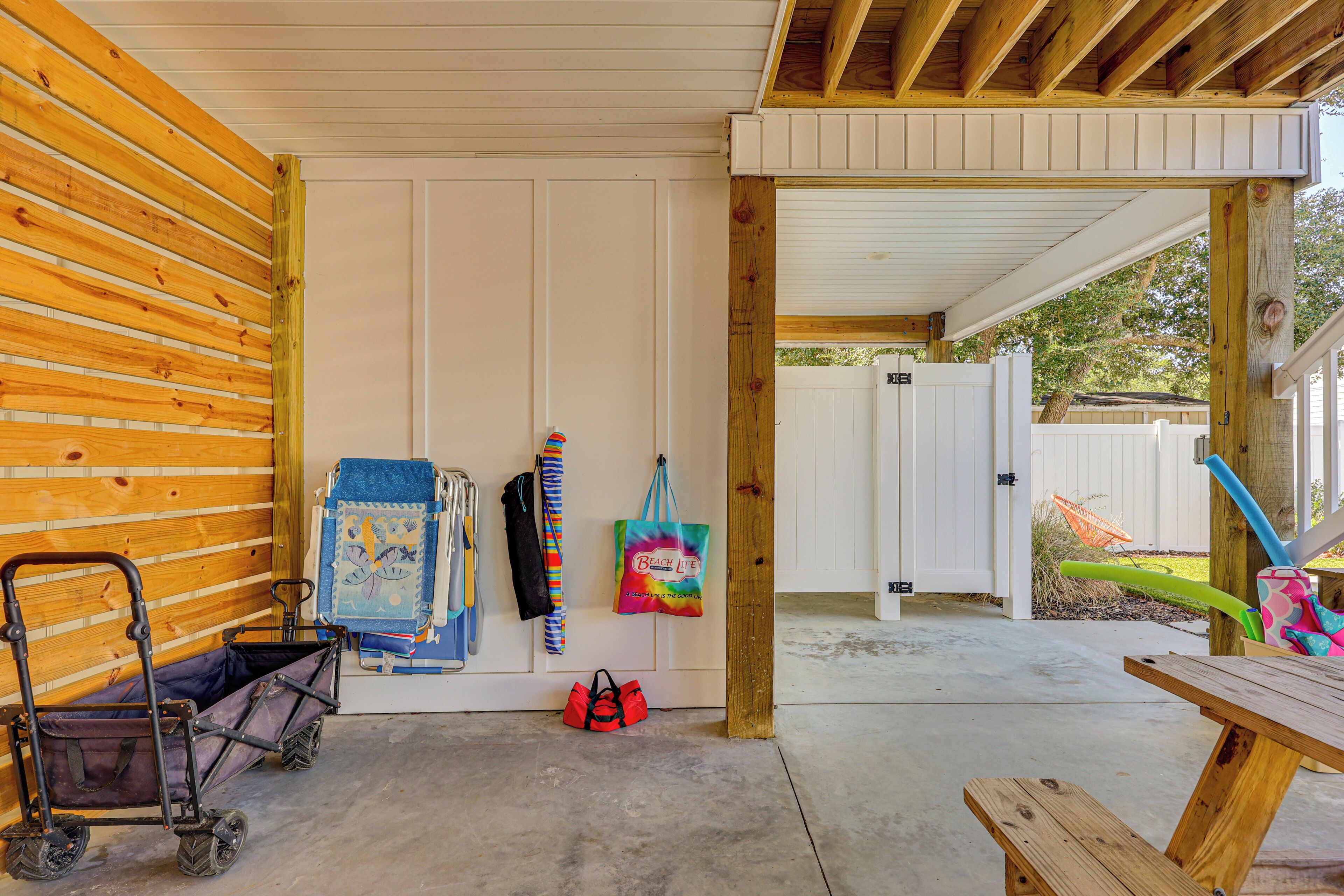 A covered outdoor area with a wooden bench, a cart, and a door leading to a fenced backyard.