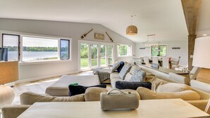 A spacious living room with a large window offering a view of a lake, a cozy seating area with a sofa and ottoman, and a dining area with a table and chairs.