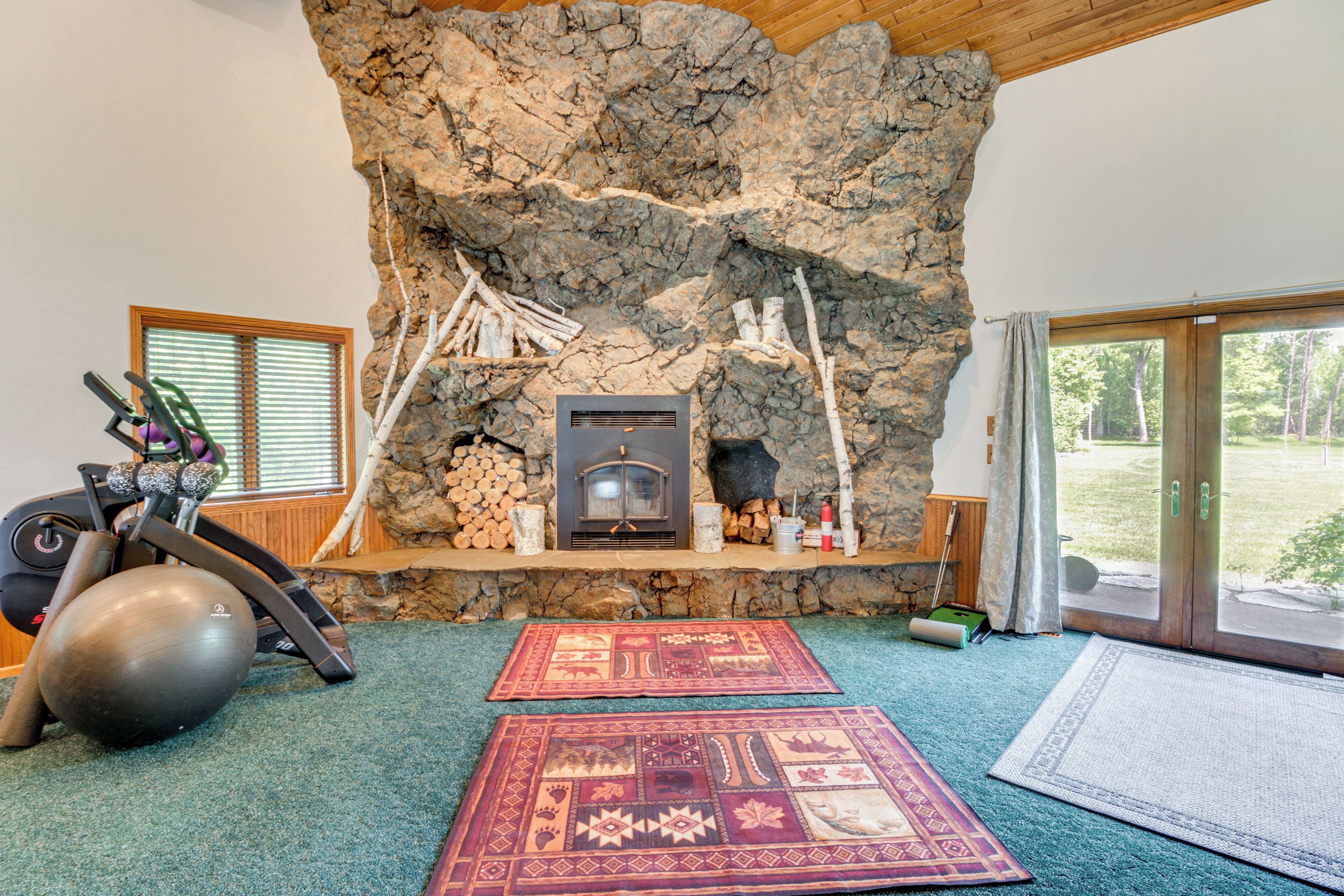 A room with a stone fireplace, exercise equipment, and two patterned rugs.