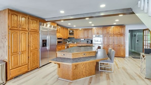 A spacious kitchen with wooden cabinets, a large island, stainless steel appliances, and a built-in seating area.