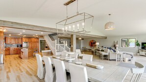 A spacious open-plan living area with a large dining table, white chairs, and a staircase leading to an upper level.