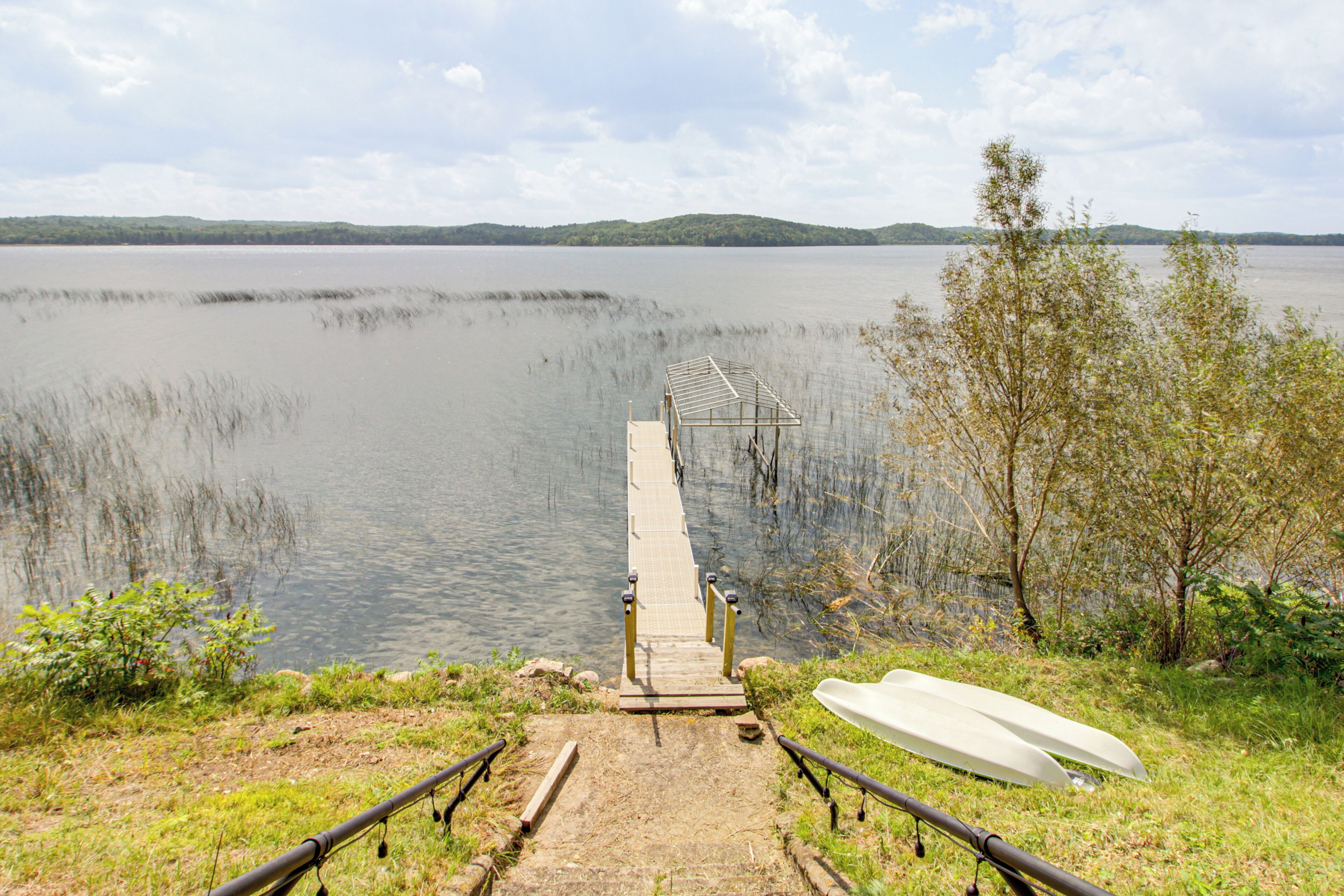A wooden dock extending into a calm lake with a boat on the shore and a distant shoreline.