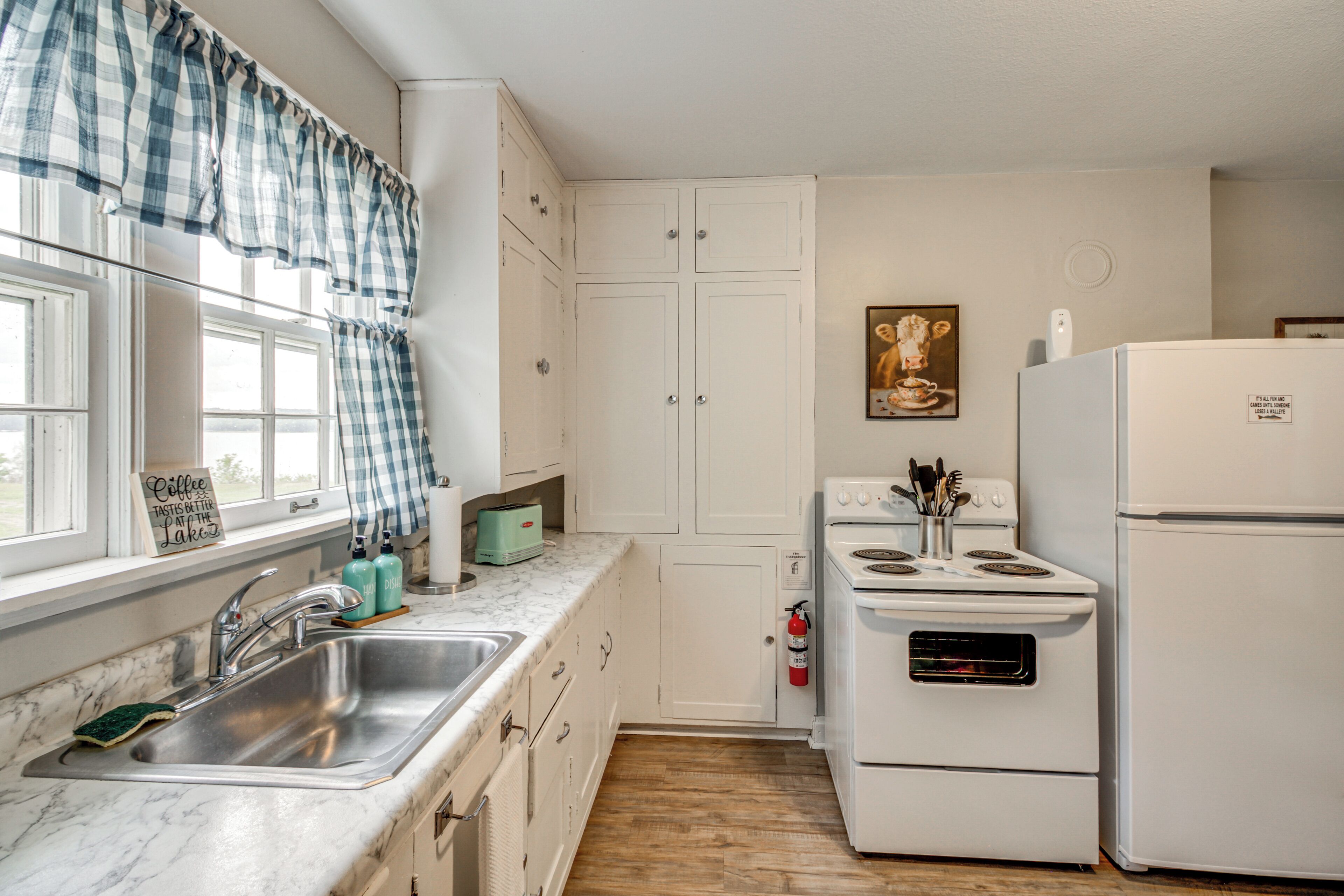 Una cocina con un lavaplatos, estufa, refrigerador y ventana con cortinas.