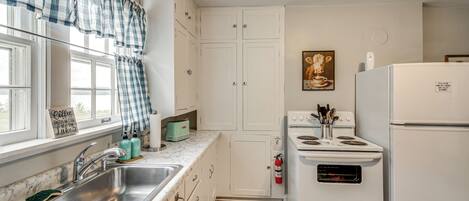 Una cocina con un lavaplatos, estufa, refrigerador y ventana con cortinas.