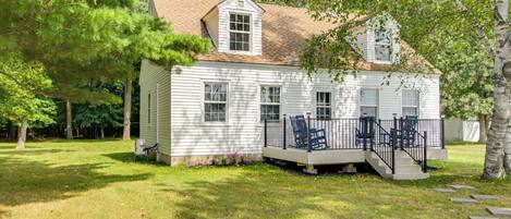 A white two-story house with a porch and steps, surrounded by trees and grass.