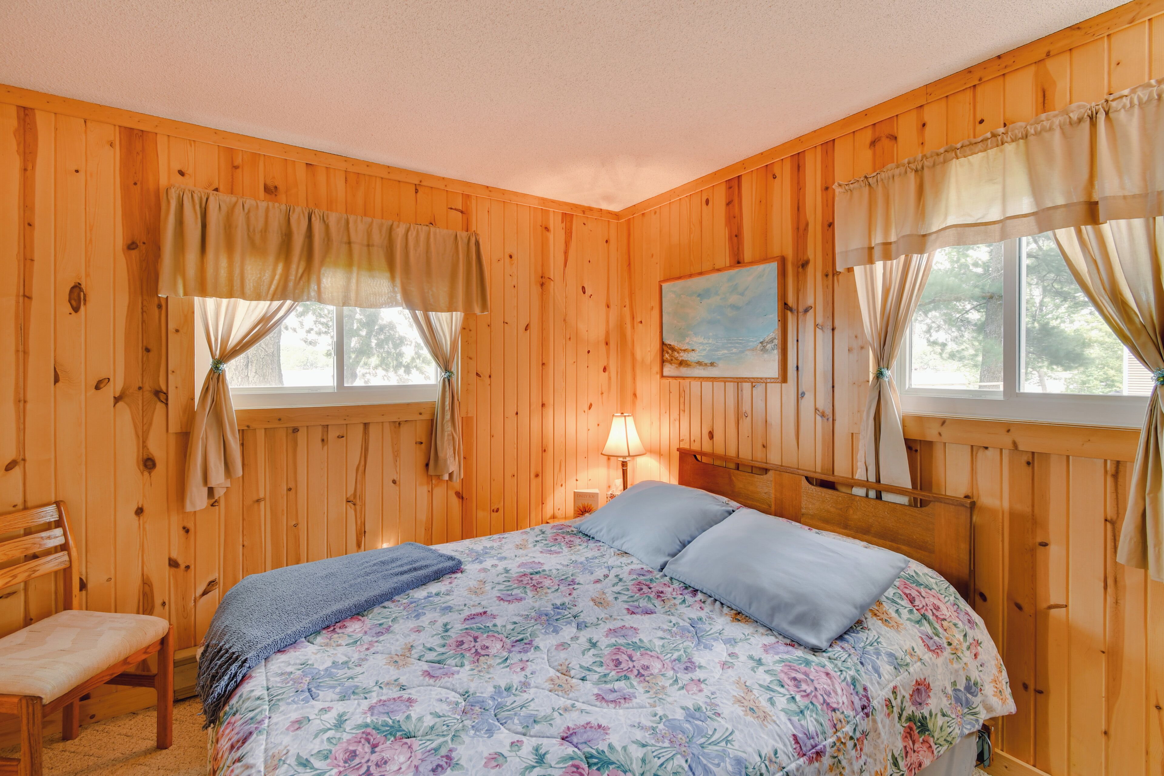 Een houten slaapkamer met een bed, een stoel en een schilderij aan de muur.