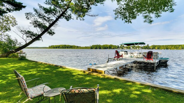 Un molo sul lago con una barca, una zona relax coperta e sedie da giardino.