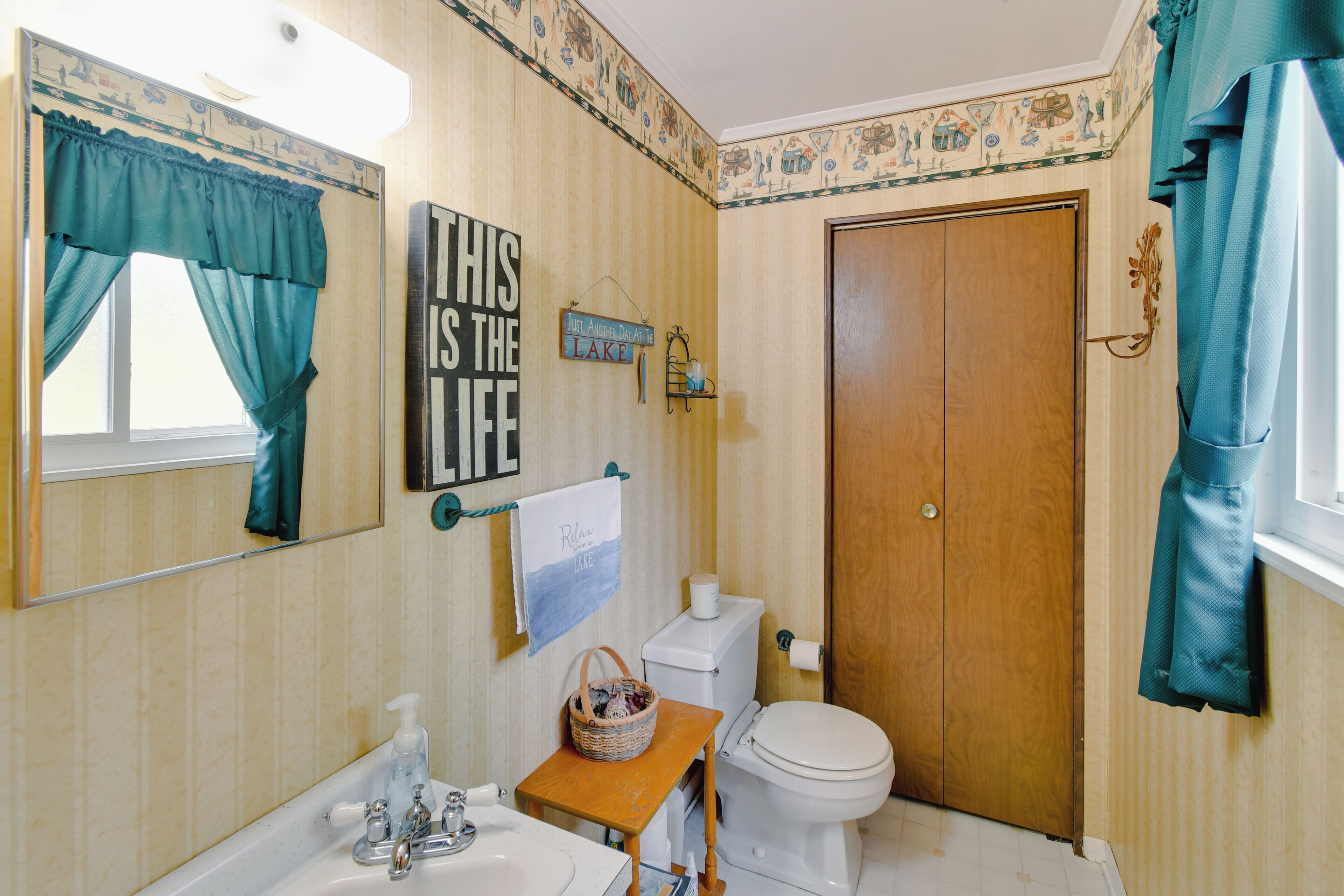 Un bagno con porta in legno, un water, un lavandino con specchio e tende color acquamarina.