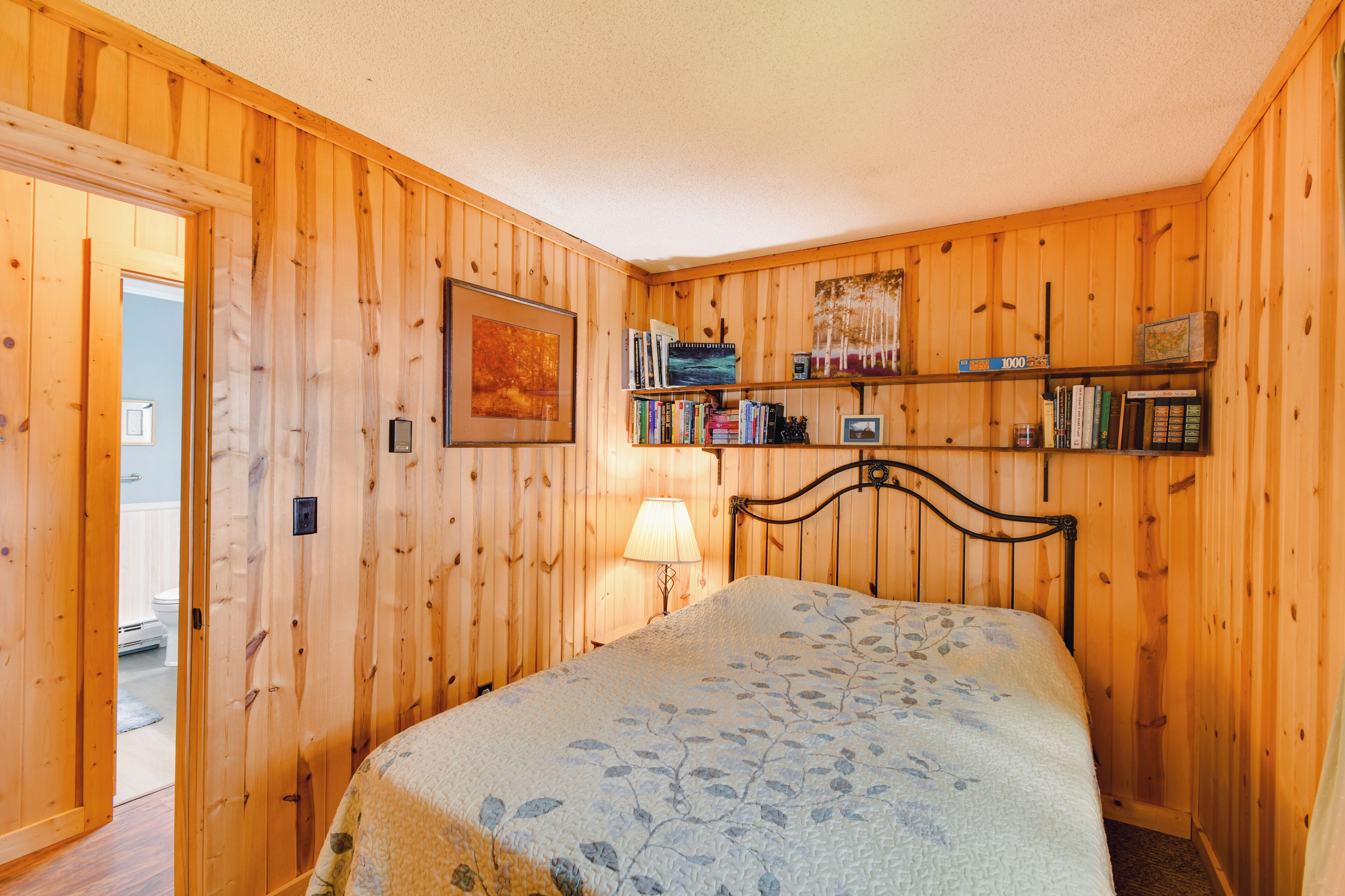 A wooden-paneled room with a bed, a bookshelf, and a framed picture on the wall.
