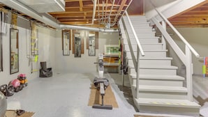 Un gimnasio en casa con equipo de ejercicio, una escalera y tuberías del techo a la vista.