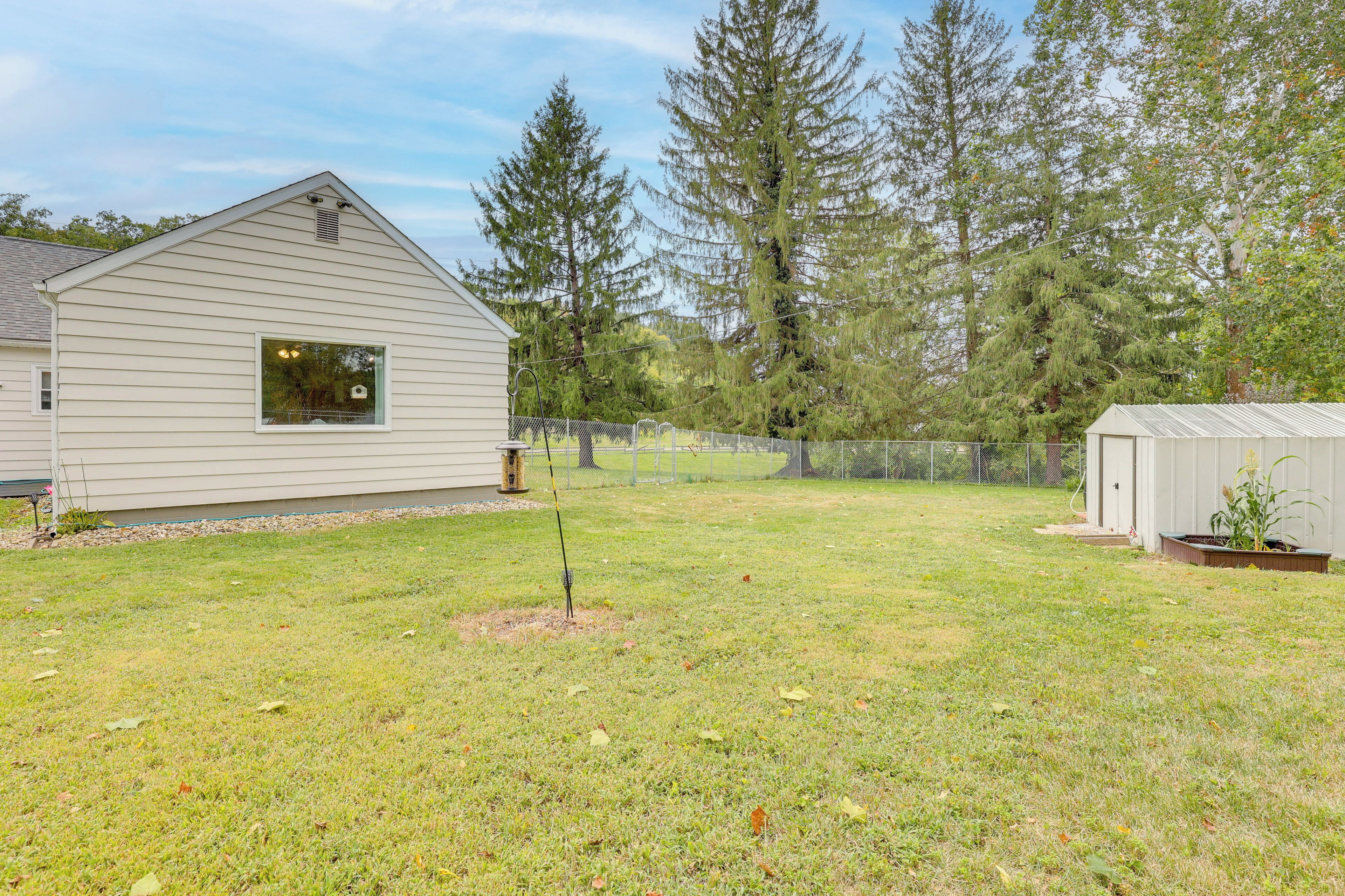 A house with a sloped roof and a window. There is a fenced yard with grass and trees.