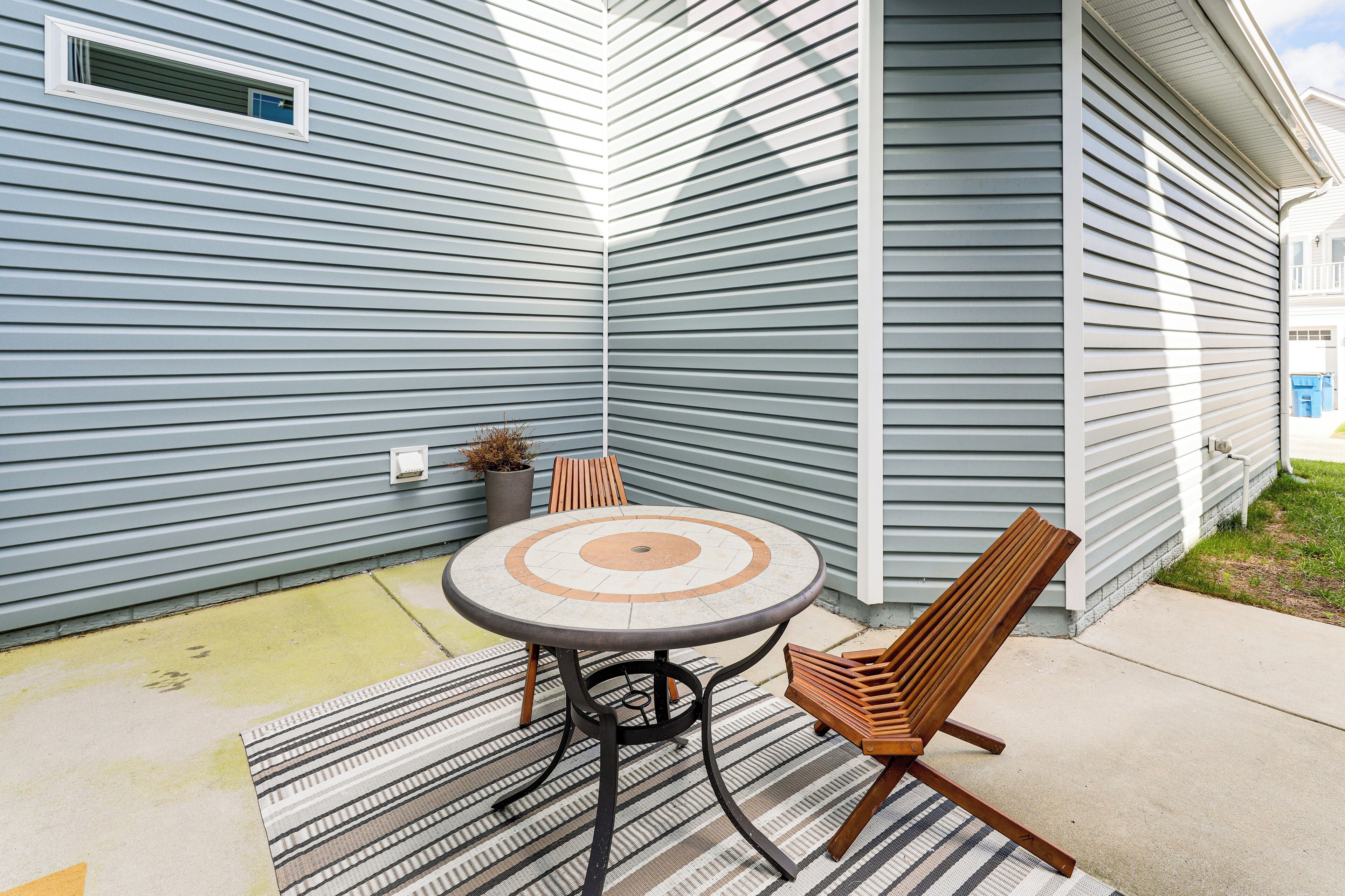 A patio with a round table and two wooden chairs, a potted plant, and a striped rug.