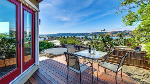 Une terrasse avec une table et des chaises, offrant une vue panoramique sur des collines et un plan d’eau.