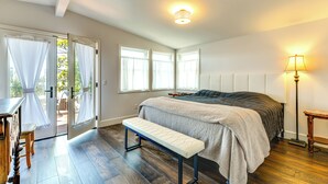 Une chambre à coucher avec un lit, un banc, une lampe de chevet et une vue sur l’extérieur, visible à travers une porte.