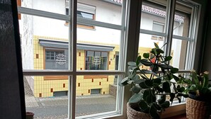 A window with a view of a building with a sign 'Carmen's Dorfladen' and a potted plant on the windowsill. - Apartment 'Child-Friendly at the Village Shop' with Private Terrace and Wi-Fi (Blankenheim)