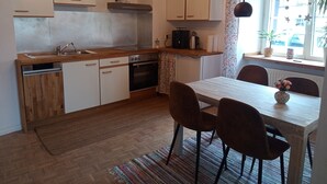 A modern kitchen with wooden cabinets, a built-in oven, and a dining area with a table and chairs. - Apartment 'Child-Friendly at the Village Shop' with Private Terrace and Wi-Fi (Blankenheim)