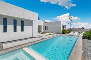 Ein modernes Gebäude mit Swimmingpool, Sitzgelegenheiten im Freien und blauem Himmel.